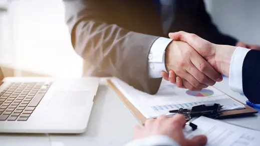 image of two professionals shaking hands over paperwork